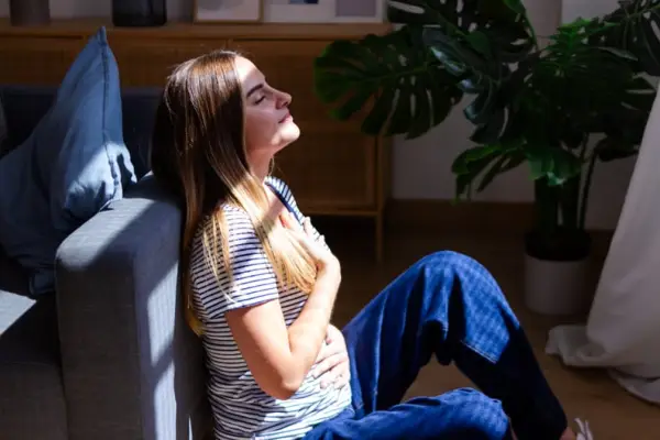 Young woman is feeling calm and relaxed while practicing breathing at home.