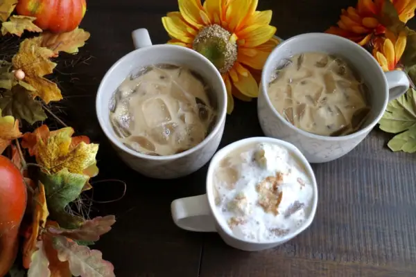 Three homemade pumpkin spice lattes in white mugs surrounded by festive fall foliage.