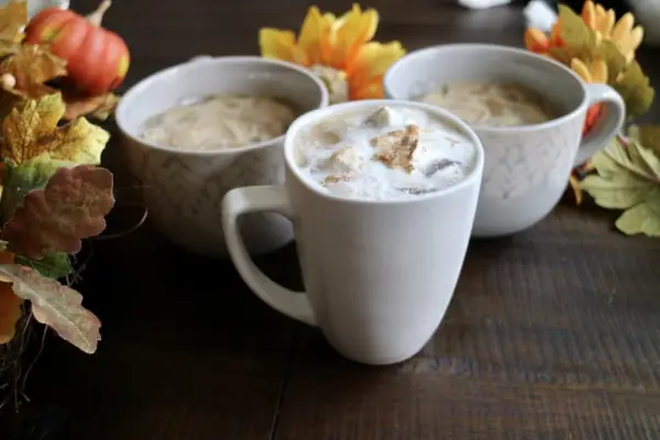 Frothy pumpkin spice lattes in white mugs surrounded by fall foliage.