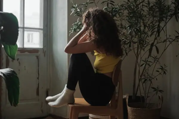 Lonely woman sitting on chair looking through window feeling sad and depressed.