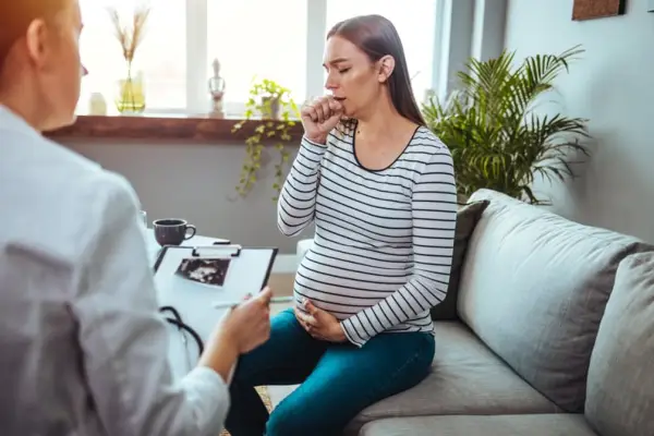 Female doctor doing a medical examination. The focus is on the young pregnant woman being examined. Young pregnant woman on a visit to doctor. Having chest pain and breathing issues.