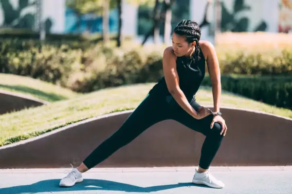 Woman in tight, black leggings and white sneakers stretches outdoors.