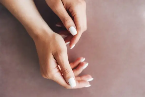 Female hands with a neat white manicure on a beige background. Beautiful female manicure.