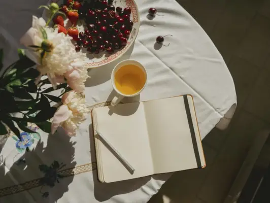 Blank Journal on a Table With White Table Cloth, Fruit, and Flowers
