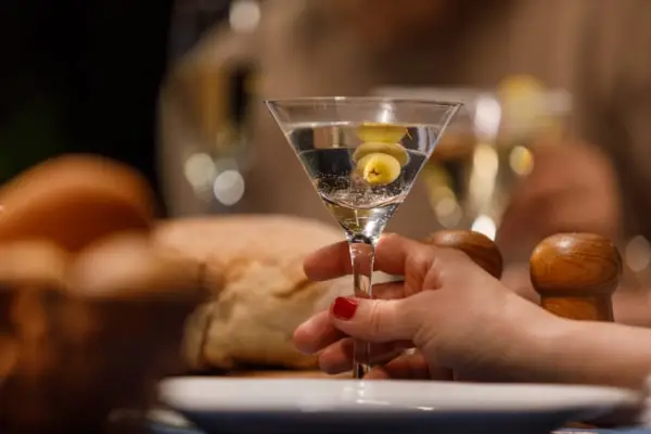 Close up shot of unrecognizable woman enjoying a martini with green olives during a dinner party with friends.