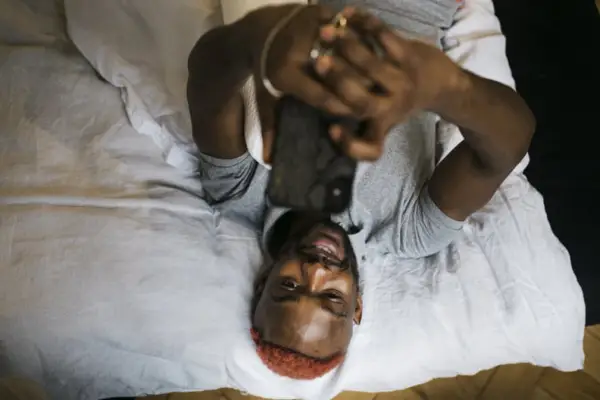 man laying on his bed holding his phone above his head and smiling