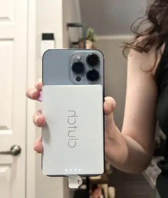 woman holding her iPhone with the Clutch Pro Lightning Portable Charger attached to in front of a mirror