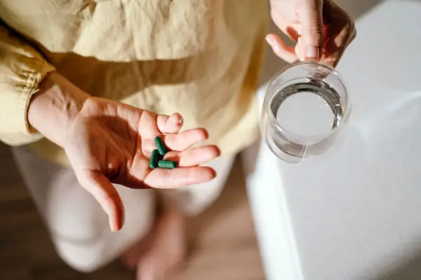A woman standing at a table with green pills in her hand, sea moss supplements.